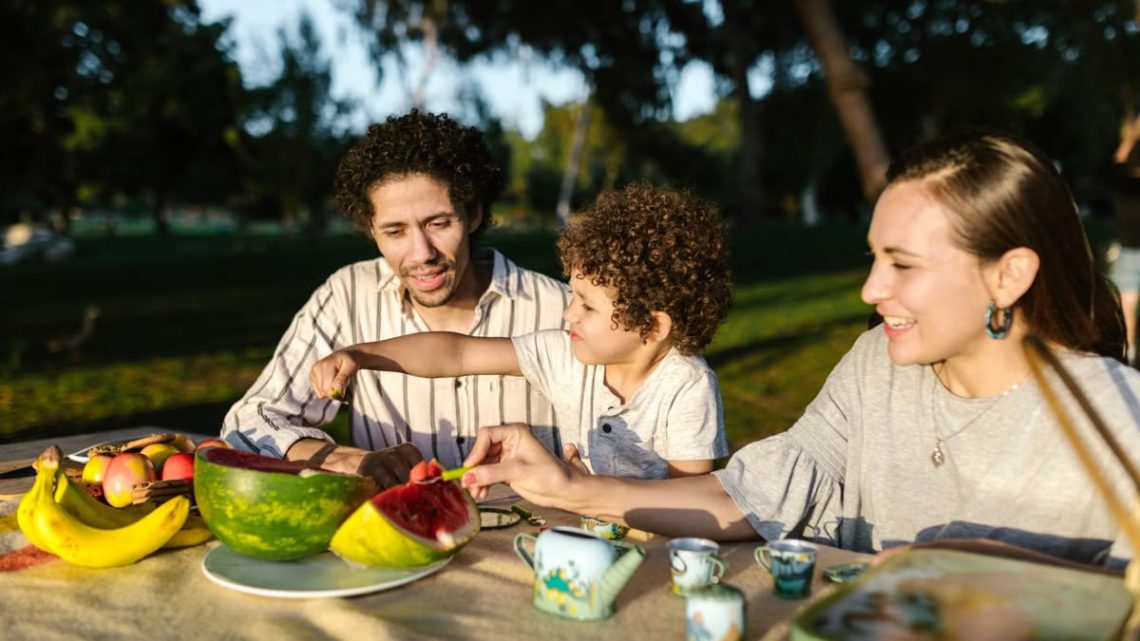 Happy family having a joyful picnic with fruits and snacks in a park during summer.