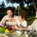Happy family having a joyful picnic with fruits and snacks in a park during summer.